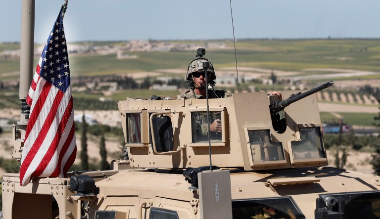 A U.S. soldier sits in an armored vehicle on a road leading to the tense front line with Turkish-backed fighters, in Manbij, north Syria, Wednesday, April 4, 2018. President Donald Trump expects to decide "very quickly" whether to remove U.S. troops from war-torn Syria, saying their primary mission was to defeat the Islamic State group and "we've almost completed that task."