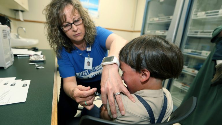 In this Friday, May 17, 2019 photo, Starr Roden, left, a registered nurse and immunization outreach coordinator with the Knox County Health Department, administers a vaccination to Jonathan Detweiler, 6, at the facility in Mount Vernon, Ohio. States are debating whether to make it more difficult for students to avoid vaccinations for religious or philosophical reasons amid the worst measles outbreak in decades, but children using such waivers are outnumbered in many states by those who give no excuse for lacking shots.Data reported to the Centers for Disease Control and Prevention shows a majority of unvaccinated or undervaccinated kindergartners in 10 of 27 states reporting were allowed to enroll in school without any exemption. 