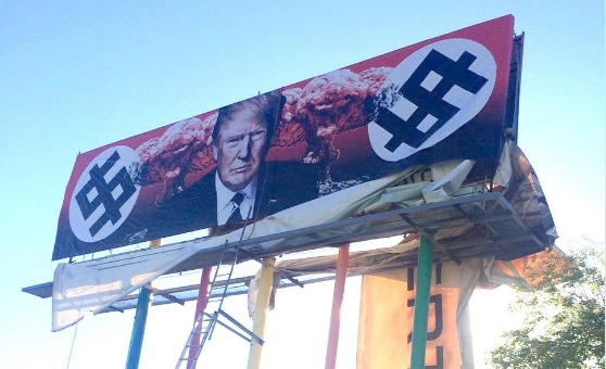 The billboard that went up Friday and features a photo of Trump's face flanked by what appear to be nuclear mushroom clouds and dollar signs that resemble swastikas. (Photo courtesy of Karen Fiorito, via Twitter)