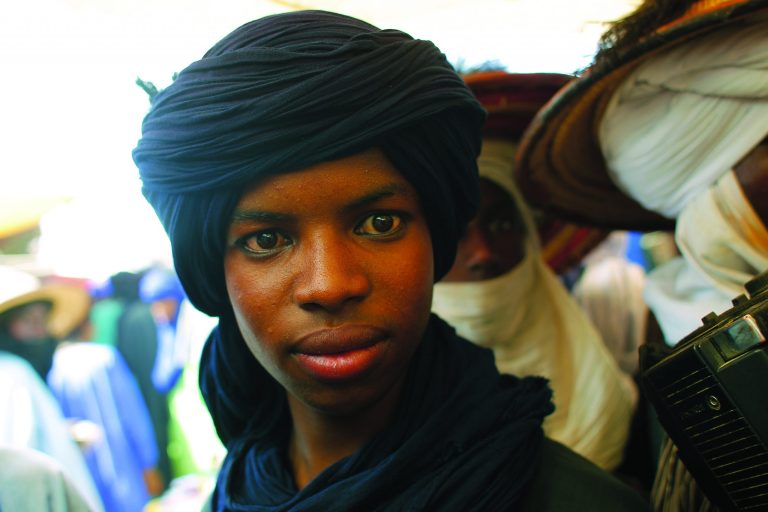 In this picture taken Tuesday, July 17, 2012, a Peul nomad stares at a visitor's camera as he and others shop for fabric and other goods while attending the livestock market in Bermo, Niger, 200 kms (125 miles) north of Maradi. This is a region where it is in livestock that a man settles disputes, pays the dowry for his future bride and leaves inheritance to his sons. For generations, nomads have lived in a precarious equilibrium with the sky above them. When the first rains come, they head north toward the Sahara desert, where the grass is said to be saltier, packed with minerals. They time their movements according to the clouds, waiting for the second major downpour, before making a U-turn to head back to the greener south. (AP Photo/Jerome Delay)