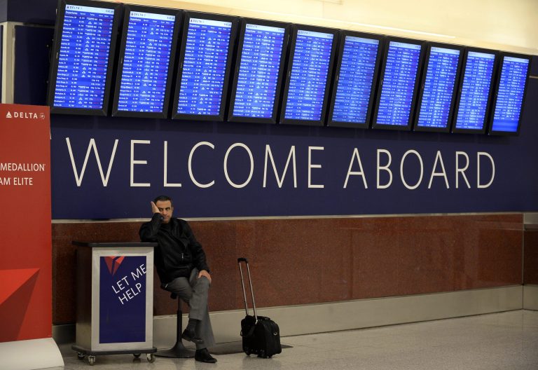 FILE - This Feb. 11, 2014 file photo shows an airline passenger waiting for his rescheduled flight to Orlando under the departure board showing hundreds of cancellations at Hartsfield-Jackson International Airport in Atlanta. Airlines should be required to disclose fees for basic services like checked bags, an assigned seat and a carry-on bag wherever tickets are sold so that passengers know the true cost of airfares, the government said Wednesday. Under new regulations proposed by the Department of Transportation, information on fees must be provided wherever passengers can purchase an airfare, including on a website, by telephone, or in-person. (AP Photo/David Tulis, File)