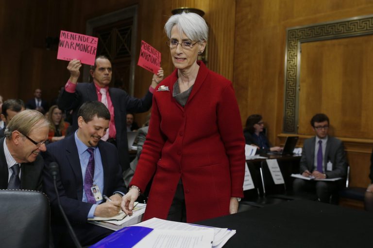 An anti war protestor holds up signs as Undersecretary of State for Political Affairs Wendy Sherman arrives on Capitol Hill in Washington, Tuesday, Feb. 4, 2014, to testify before the Senate Foreign Relations Committee hearing examining negotiations on Iran's nuclear program.  (AP Photo/Charles Dharapak)