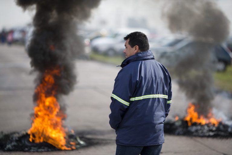 A worker stands next to burning tires outside the entrance of RR Donnelley printing plant in the outskirts of Buenos Aires, Argentina, Monday, Aug. 11, 2014. RR Donnelley, a Fortune 500 company from Chicago, closed its plant in Argentina without warning catching its 400 workers by surprise when they showed up for work Monday morning. The company posted a letter outside it's entrance announcing its closing due to 