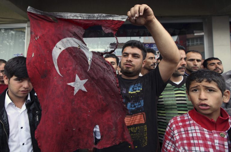 Turkish people display a damaged national flag found in the debris of a destroyed shop as they stage an anti-government protest near the scene at one of the Saturday explosion sites that killed 46 and injured about 50 others, in Reyhanli, near Turkey's border with Syria, Monday, May 13, 2013. Prime Minister Recep Tayyip Erdogan said Monday Turkey would 