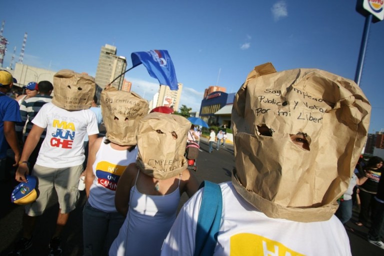 Government workers who support Henrique Capriles, the challenger to Hugo Chavez, wearing masks at a public rally in order to avoid reprisals. The paper-bag masks read, 