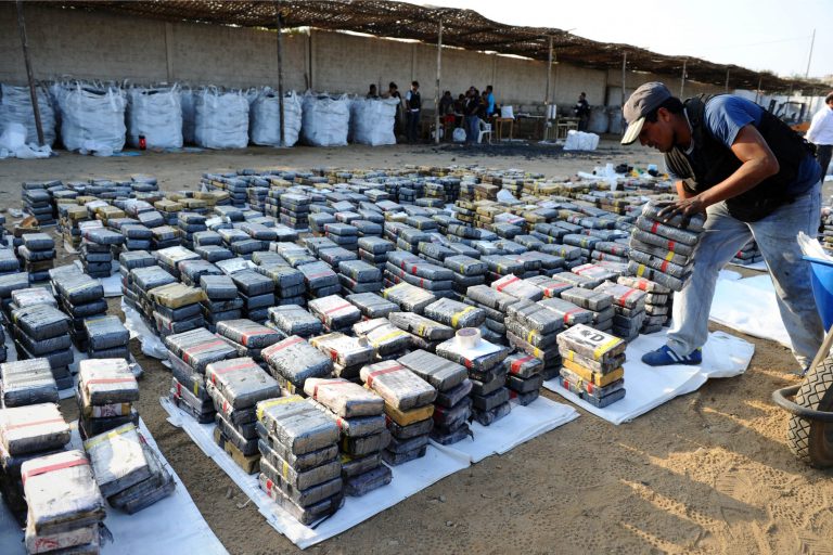 In this photo provided by Peru's Interior Ministry, a police officer arranges blocks of cocaine for display to the press, in Trujillo Peru, Tuesday, Aug. 26, 2014. Peruvian police say they have seized at least 3.3 tons of cocaine, the year's biggest haul, hidden in a shipment of coal that was bound for Belgium and Spain. (AP Photo/Peru's Interior Ministry)