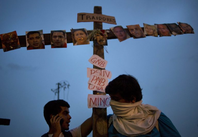 Anti-government protesters carry a cross covered with photos of government officials and supporters under the Spanish word 