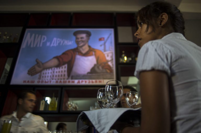 In this Aug 20, 2014 photo, a waitress works during the pre-launch rehearsal at the new restaurant Nazdarovie where the reproduction of Soviet propaganda poster hangs over the bar area in Havana, Cuba.  The new retro-Soviet restaurant serves minty mojitos, but they come mixed with vodka instead of the traditional white rum. (AP Photo/Ramon Espinosa)