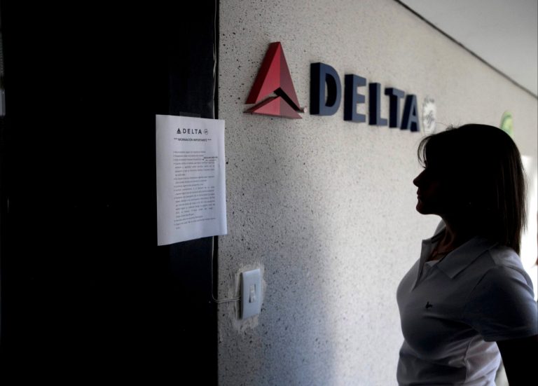 FILE - In this Jan. 24, 2014 file photo, a woman reads a notice on the door of a closed Delta Airlines office after the government devalued the local currency for flights abroad in Caracas, Venezuela. Delta spokeswoman Sarah Lora confirmed Monday, July 7, 2014 that the carrier is reducing service by 85 percent, replacing its daily roundtrip flight between Atlanta and Caracas with one roundtrip weekend flight as of Aug. 1. (AP Photo/Alejandro Cegarra, File)