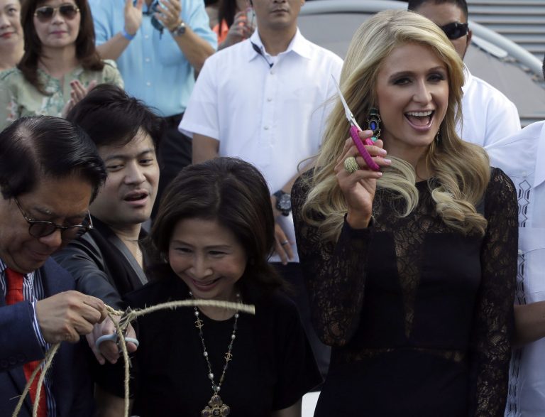 Paris Hilton, right, waves a pair of scissors after cutting the ribbon in the ceremony to unveil the Paris Beach Club, which she designed in collaboration with Philippine developer Century Properties, Thursday, March 13, 2014 at suburban Paranaque city, southeast of Manila, Philippines.  Paris Hilton unveiled her first real estate project Thursday in metropolitan Manila and said she wants to follow in the footsteps of her great-grandfather and grandfather, who led a luxury hotel empire. (AP Photo/Bullit Marquez)