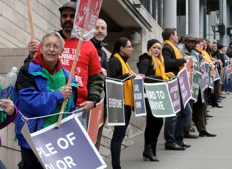 Paula Lukaszek, left in blue jacket, and other supporters of a measure to raise the minimum wage to $15 an hour surround Seattle City Hall for about 40 minutes Wednesday afternoon, April 23, 2014. Lukaszek is a plumber at the University of Washington and president of Local 1488 WFSE - Washington Federation of State Employees. She makes more than $15 per hour but is there in support of those who don't.  (AP Photo/The Seattle Times, Greg Gilbert)  SEATTLE OUT; USA TODAY OUT; MAGS OUT; TELEVISION OUT; NO SALES; MANDATORY CREDIT TO BOTH THE SEATTLE TIMES AND THE PHOTOGRAPHER