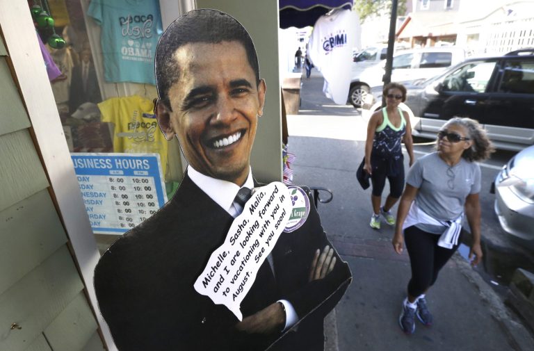 Passers-by walk near a cut-out of President Barack Obama, left, outside a shop Saturday, Aug. 9, 2014, in Oak Bluffs, Mass., on the island of Martha's Vineyard. President Obama and his family are returning to the island off the Massachusetts mainland Saturday. The president is doing something unusual with his summer vacation on Martha's Vineyard: He'll come back to Washington midway through the getaway to attend White House meetings. (AP Photo/Steven Senne)