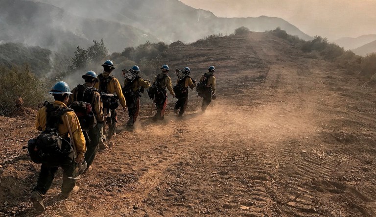 In this photo provided by the Santa Barbara County Fire Department, U.S. Forest Service Hot Shot crew members from Ojai, Calif., head down a fire break to work off E. Camino Cielo in Santa Barbara, Calif., Sunday morning, Dec. 17, 2017. Thousands of firefighters tried Sunday to shield coastal communities from one of the biggest wildfires in California history while a funeral procession rolled past burn-scarred hillsides in honor of one of their colleagues who was killed battling the flames. (Mike Eliason/Santa Barbara County Fire Department via AP)