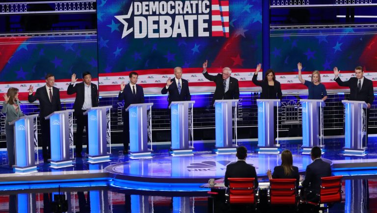 In this June 27, 2019 photo, Democratic presidential candidates, author Marianne Williamson, former Colorado Gov. John Hickenlooper, entrepreneur Andrew Yang, South Bend Mayor Pete Buttigieg, former Vice President Joe Biden, Sen. Bernie Sanders, I-Vt., Sen. Kamala Harris, D-Calif., Sen. Kirsten Gillibrand, D-N.Y., Colorado Sen. Michael Bennet, and Rep. Eric Swalwell, D-Calif., raise their hands when asked if they would provide healthcare for undocumented immigrants, during the Democratic primary debate hosted by NBC News at the Adrienne Arsht Center for the Performing Arts in Miami. 