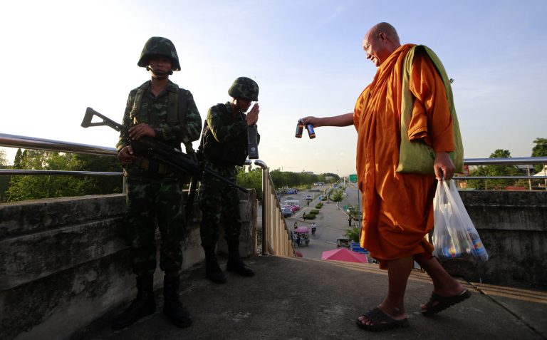 A Buddhist monk offers energy drink to Thai soldiers guarding a pedestrian overfly near the site where pro-government demonstrators stage a rally on the outskirts of Bangkok, Thailand Tuesday, May 20, 2014. As Thailand finishes its first day under martial law, there are some questions that the military action raises. Many wonder if the arrival of soldiers in the streets of Bangkok constitutes a military coup, and how it affects people living in the Thai capital or visiting.  (AP Photo/Wason Wanichakorn)