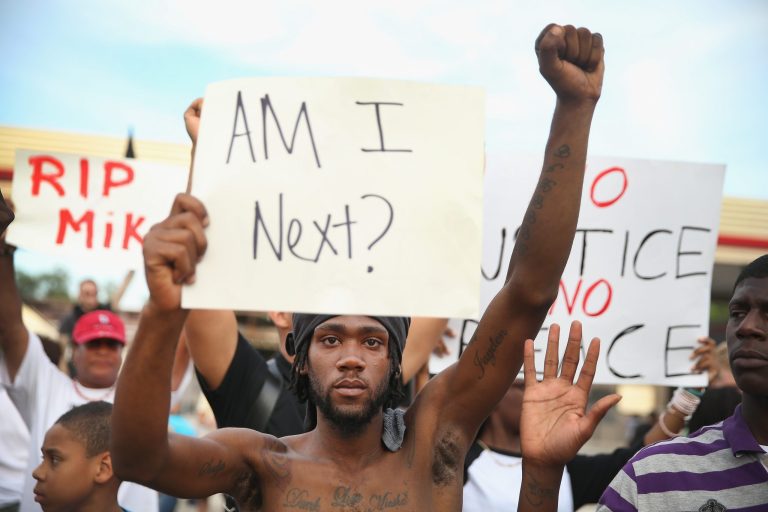 Demetrus Washington joins other demonstrators protesting the shooting death of teenager Michael Brown on August 14, 2014 in Ferguson, Missouri. Brown was shot and killed by a Ferguson police officer on August 9. Police in Ferguson have changed their procedure for dealing with the protests after being chastised for a heavy-handed approach which has resulted in four days of violence. Today three police cars and four officers on foot led the way during a protest march. (Photo by Scott Olson/Getty Images)
