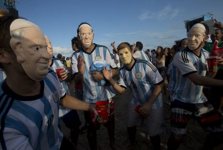 Soccer fans of the Argentina national soccer team wear masks with faces of Pope Francis and Argentine soccer player Lionel Messi during a live telecast of the soccer World Cup semifinal match between Argentina and Netherlands, inside the FIFA Fan Fest area on Copacabana beach, in Rio de Janeiro, Brazil, Wednesday, July 9, 2014. (AP Photo/Silvia Izquierdo)