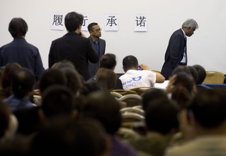 Bala Chandran Tharman, right, deputy chief of mission at the Malaysian embassy in Beijing walks away while relatives of Chinese passengers onboard the Malaysia Airlines MH370 ask him a question during a briefing at a hotel in Beijing, China, Saturday, April 26, 2014. A number of Chinese relatives still aren't accepting the theory that the plane crashed in the Indian Ocean. They're insisting that Malaysian officials haven't told them the truth. The Chinese characters on the wall reads: 