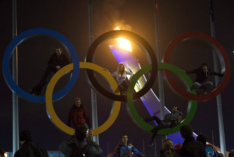 People climb the Olympic Rings as the Olympic cauldron burns in the background at the 2014 Sochi Winter Olympics in Sochi, Russia, on Friday. (AP Photo/The Canadian Press, Nathan Denette)