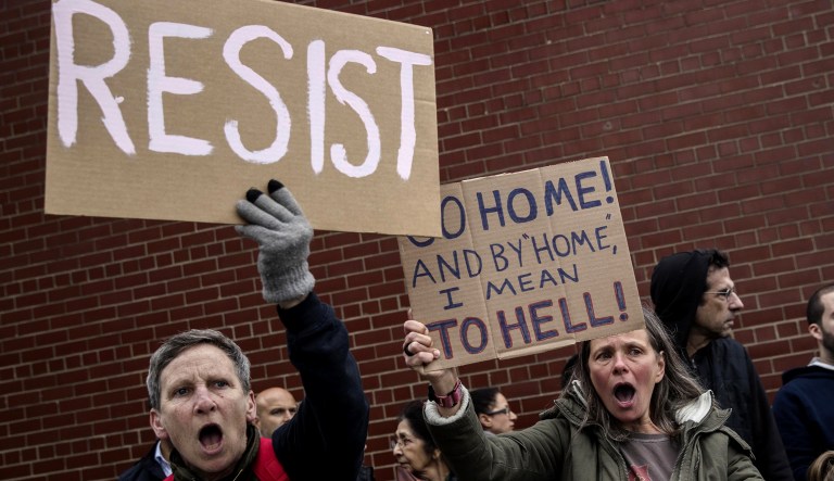 Demonstrators hold signs while protesting against President Trump.