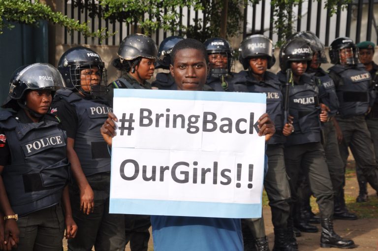 A man poses with a sign in front of police officers in riot gear during a demonstration calling on the government to rescue the kidnapped girls of the government secondary school in Chibok, in Abuja, Nigeria, Tuesday\. Scores of protesters marched chanting 