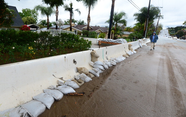 A man walks past sandbags place in front of a retaining wall in a Glendora neighborhood on the foothills of the San Gabriel Mountains east of Los Angeles on February 28, 2014 in California. (FREDERIC J. BROWN/AFP/Getty Images)