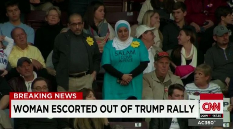 A Muslim man and woman, who were standing in protest at a Trump rally, seem to be escorted out by police. (CNN/Screengrab)