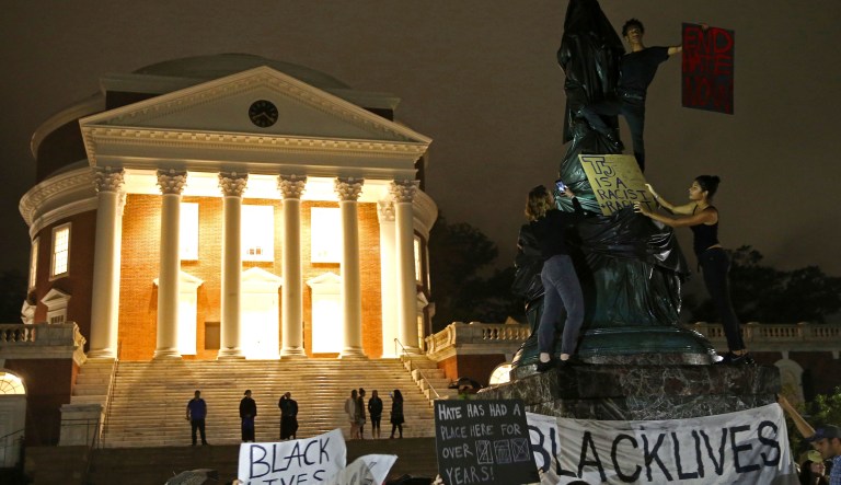 Protesters cover a statue of Thomas Jefferson with black tarp and hold signs up in front of the Rotunda at the University of Virginia for the one month anniversary of the 