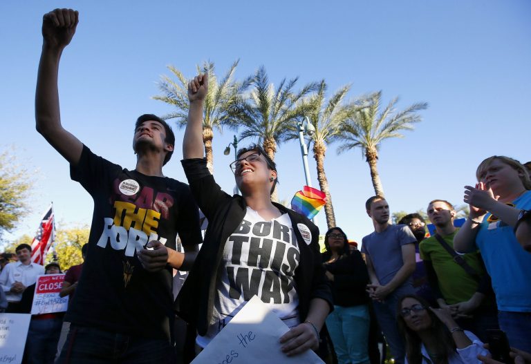 Anthony Musa, left, and Brianna Pantillione join nearly 250 gay rights supporters protesting SB1062 at the Arizona Capitol, Friday, Feb. 21, 2014, in Phoenix.  The protesters gathered demanding Gov. Jan Brewer veto legislation that would allow business owners to refuse to serve gays by citing their religious beliefs.  The governor must sign or veto Senate Bill 1062 by the end of next week. (AP Photo/Ross D. Franklin)