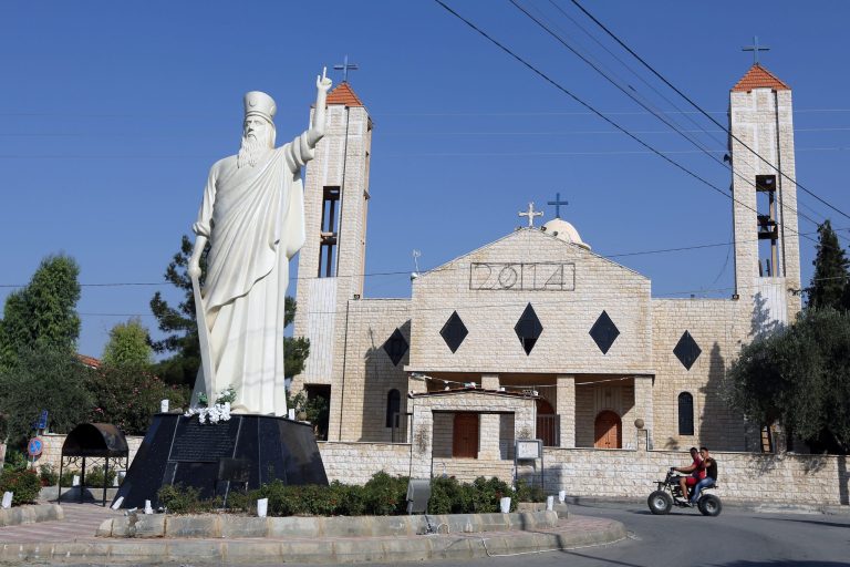 In this Wednesday, Aug. 13, 2014 photo, two young men ride a motorcycle past a church in Lebanon's Christian village of Ras Baalbek in the northern Bekaa region near the border with Syria. Across the Middle East, Christian communities as old as the religion itself feel their very survival is at stake, threatened by militants of the Islamic State group rampaging across Iraq and Syria. Many Christian villagers are setting up self-defense units to protect themselves against attack. In Qaa and Ras Baalbek, two Christian northeastern villages on the border with Syria, many of the thousands of expatriates who used to spend the summer there stayed away this year. (AP Photo/Bilal Hussein)