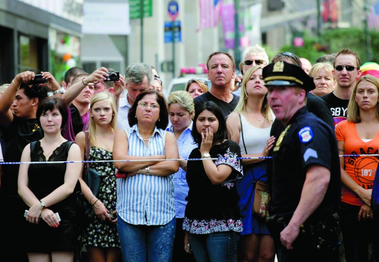 FILE - In this Aug. 24, 2012, file photo, bystanders and a police officer stand on Fifth Avenue to view the scene outside the Empire State Building after a fatal shooting in New York. While recent shootings at a Colorado movie theater, a Sikh temple and outside the Empire State Building have grabbed headlines, residents of inner-city neighborhoods wracked by gun violence say they feel neglected and ignored in this presidential election year. (AP Photo/Mark Lennihan, File)