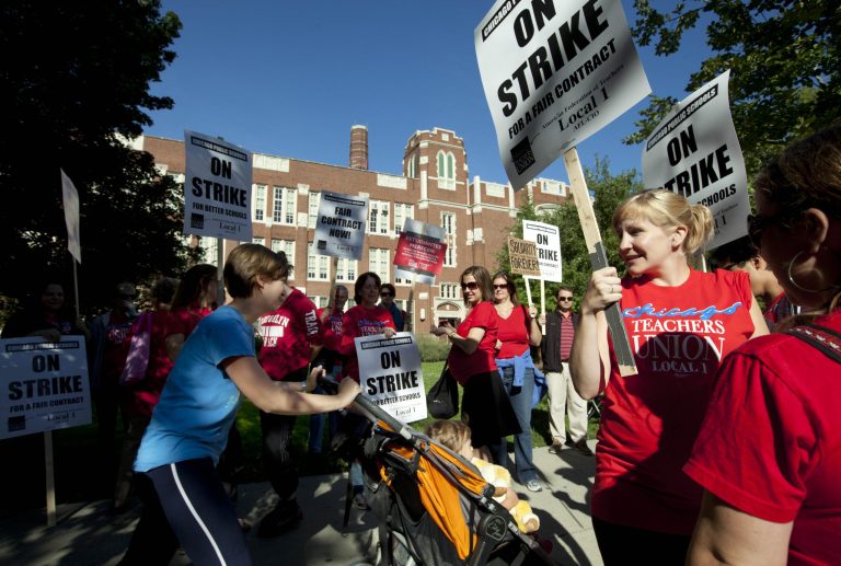 A woman pushes a stroller past a group of public school teachers picketing outside Amundsen High School in Chicago. (AP photo)