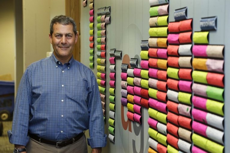In this Monday, June 23, 2014 photo, Chuck Stempler, owner of an AlphaGraphics printing and marketing franchise, poses for a photo next to a wall that tracks current jobs for customers at his business, in Seattle. Stempler, who is a plaintiff in a federal lawsuit seeking to overturn a Seattle law that will raise the city's minimum wage to $15 from the current $9.32, says he will have to cut jobs to afford the higher wage. (AP Photo/Ted S. Warren)