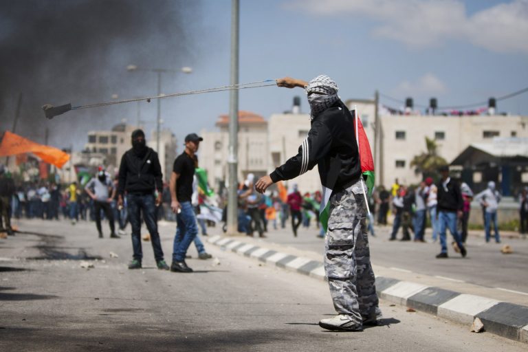 A masked Palestinian uses a slingshot to hurl stones toward Israeli soldiers during a protest calling for the release of Palestinian prisoners held in Israeli jails, outside Ofer, an Israeli military prison near the West Bank city of Ramallah, Friday, April 4, 2014. (AP Photo/Majdi Mohammed)