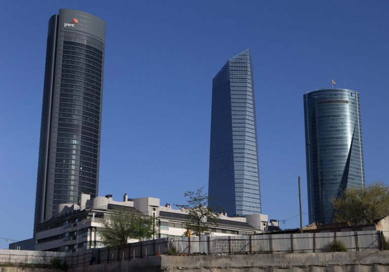 A man looks over a fence in front of office towers in the business district of Madrid, Spain, Friday, April 11, 2014. Spain's statistics office said prices were 0.1 percent lower in March than the year before, slightly less than the previous estimate of 0.2 percent. The figures released Friday by the National Statistics Institute may ease concerns that the country will suffer a prolonged bout of deflation, or falling prices. Deflation can weigh on growth by prompting consumers to delay purchases and businesses to refrain from investing. (AP Photo/Paul White)