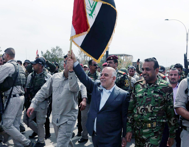 In this image posted on the official Facebook account of Iraq's Prime Minister Haider al-Abadi shows the premier carrying the national flag as he walks with Iraqi security forces in Tikrit, Iraq, Wednesday, April 1, 2015. (AP Photo/Iraq Prime Minister's office)