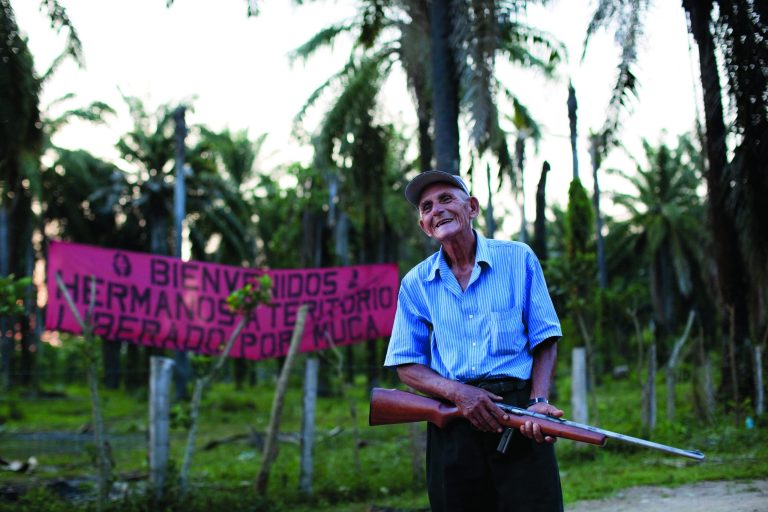 In this May 7, 2012 photo, Paulino Martinez, 71, stands guard main entrance checkpoint of La Confianza, Honduras, a city developed from land seized by small-scale farmers from one of Honduras' richest men. The collection of tin-and-wood shacks boasts a health center, a school, a meeting hall, and a store. The land seizure has spawned a violent land conflict between the farmers and owner, billionaire Miguel Facusse, that has killed at least 63 people, mostly peasants, in the last three years in the Bajo Aguan Valley. (AP Photo/Rodrigo Abd)