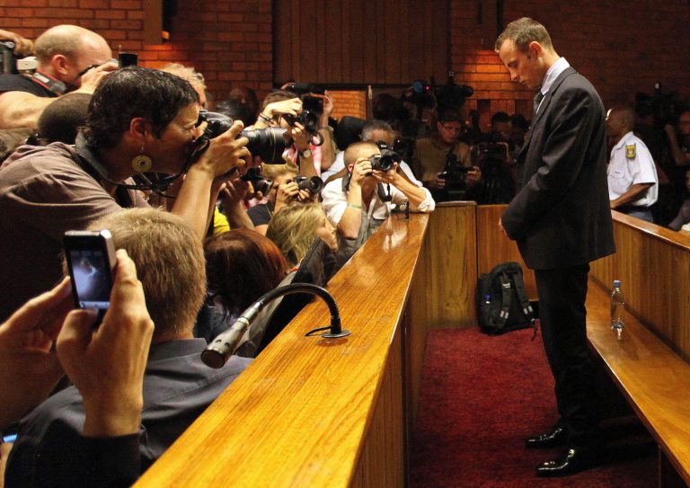 FILE - In this Wednesday, Feb. 20, 2013 file photo Olympic athlete Oscar Pistorius stands inside a court during his bail hearing at the magistrate court in Pretoria, South Africa.  With his athletic triumphs tarnished by the killing of his girlfriend, Reeva Steenkamp. Pistorius, now 27, faces possibly being sent to prison until he is older than 50. Pistorius goes on trial Monday March 3, 2014. (AP Photo/Themba Hadebe, File)