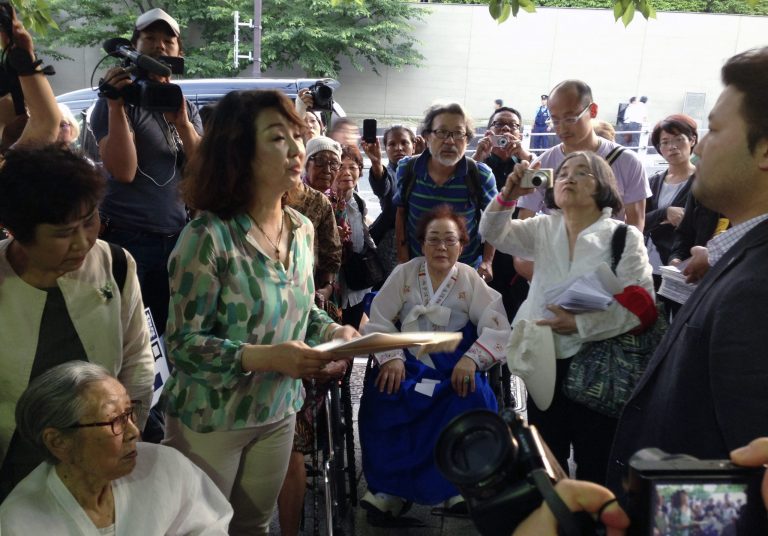 Supporter Yang Chingja, second left, hands to a government official part of hundreds of pages of documents that experts say contain proof of coercion in the military-led âcomfort womenâ sex slavery system during World War II, as former South Korean victims, Kim Bok-dong, 88, bottom left, and Lee Yong-soo, 85, center on wheelchair, and Indonesian victim Mince, 86, far back center wearing a white cap next to Yang, look on. The group demanded Prime Minister Shinzo Abe face Japanâs wartime atrocity and formally apologize. Historians who helped compile the 529 pieces of official records, collected from in and outside Japan, show clear evidence of coercion by the Japanese military and government in recruiting and running the system. (AP Photo/Mari Yamaguchi)