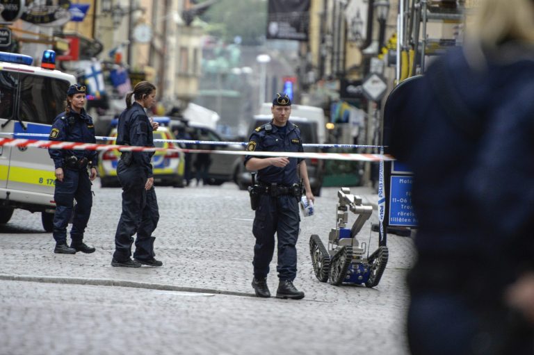 Police officers and a bomb robot stand in a cordoned off area in central Stockholm, Sweden, Thursday June 19, 2014. Stockholm police say they have closed off and evacuated parts of the city center because of threatening behavior by a man who claims he has a 