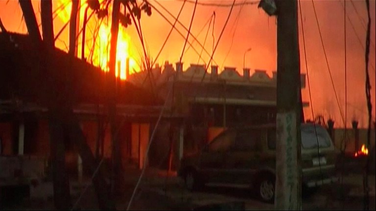 In this image taken from video, flames rise in the background of houses after a state-owned gas pipeline exploded in Nagaram village, in the southern Indian state of Andhra Pradesh  Friday, June 27, 2014. A top official of the state-run Gas Authority of India Ltd, said more than a dozen people died in the fire following the explosion in the pipeline. (AP Photo/NNIS via AP Video) INDIA OUT