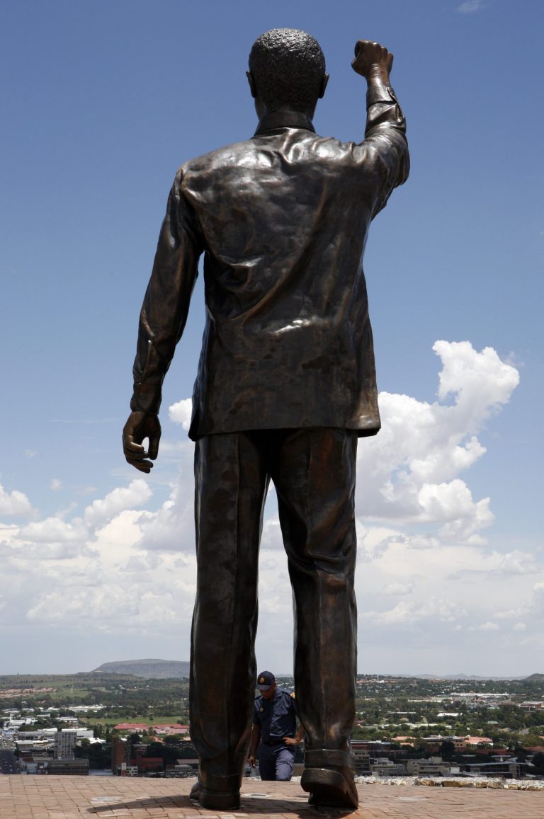   People walk next to a giant statue of former South African President Nelson Mandela on Naval Hill, overlooking the city of Bloemfontein, South Africa, on Wednesday, Dec. 19, 2012. The 94-year old anti-apartheid icon Nelson Mandela is spending a twelfth day in a South African hospital after being diagnosed with a lung infection and undergoing gallstone surgery.(AP Photo/Themba Hadebe)  