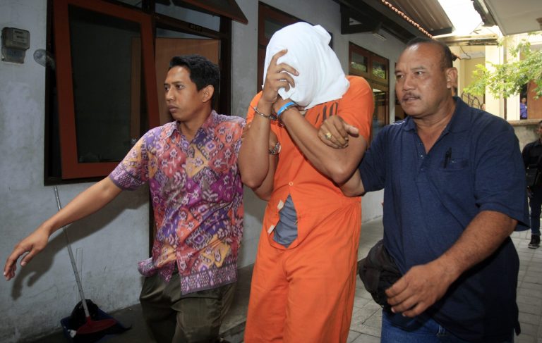 Indonesian police officers escort Tommy Schaefer, center, covering his face,  to a hospital for medical check Friday, Aug. 15, 2014.  The body of the 62-year-old American woman Sheila von Wiese-Mack was found stuffed inside a suitcase on the Indonesian resort island of Bali, and authorities on Wednesday arrested her daughter Heather Mack and her daughter's boyfriend Schaefer  in relation to the death, police said. (AP Photo/Firdia Lisnawati)