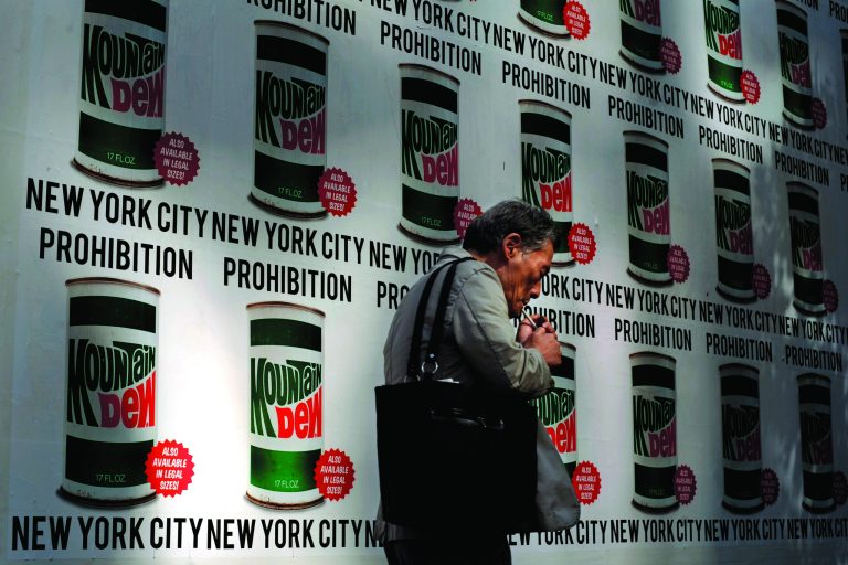 A man lights a cigarette as he walks past an advertisement created in collaboration with Mountain Dew and New York Art Department, Thursday, Sept. 13, 2012, on 13th Street in New York. New York City cracked down on supersized sodas and other sugary drinks Thursday in what is celebrated as a groundbreaking attempt to curb obesity and condemned as a breathtaking intrusion into people's lives by a mayor bent on creating a 