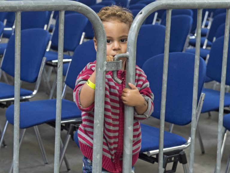 Two-year-old Weesam Srhan of Syria waits behind a protective fence in his accommodation, the exhibition halls of the Trade Fair Messe Erfurt, in Erfurt, central Germany, Tuesday, Sept. 8, 2015. (AP Photo/Jens Meyer)