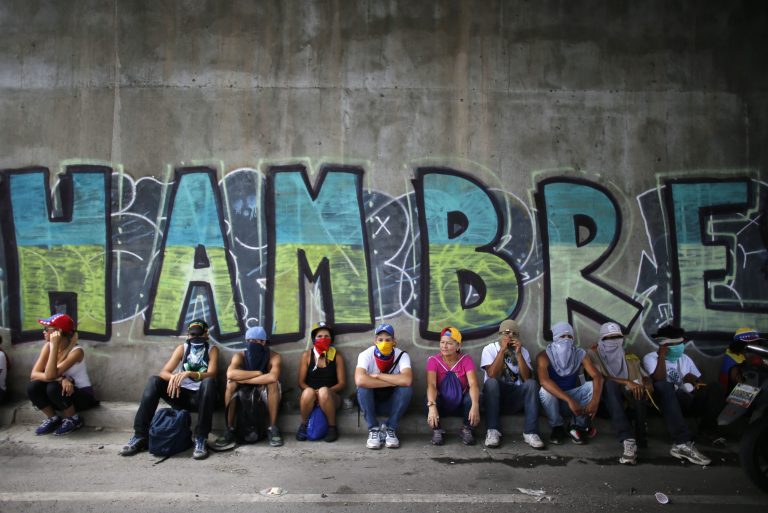 Anti-government demonstrators sit under a bridge that has graffiti written in Spanish that reads 