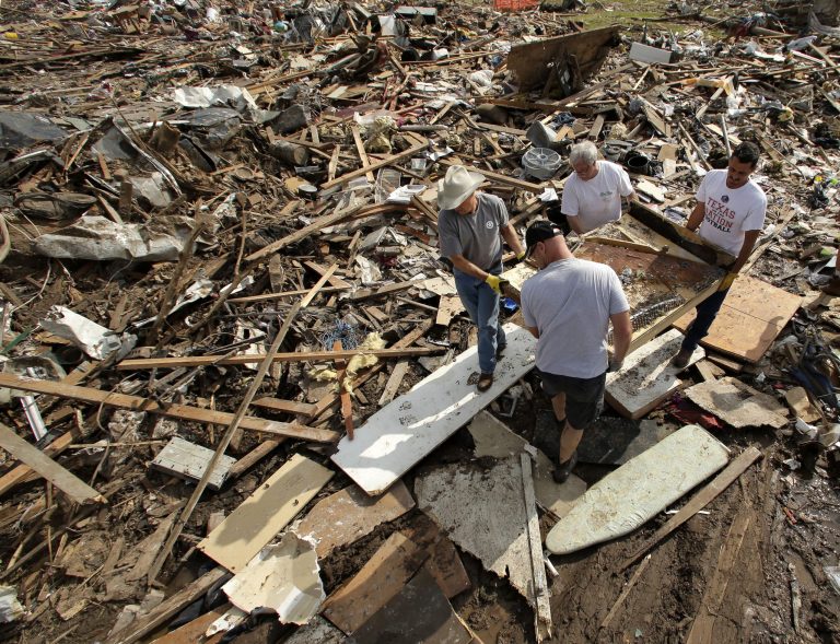 FILE - In this May 25, 2013 file photo, friends and family members carry what remains of piano through the rubble at a tornado-ravaged home, in Moore, Okla. Before construction workers can begin rebuilding the town of Moore, they have to overcome a mile-high pile of crushed wood, shattered glass, obliterated belongings and squished siding. (AP Photo/Charlie Riedel, File)