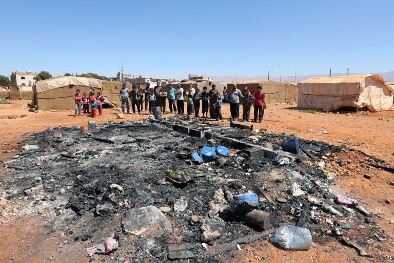 In this photo taken Wednesday, Sept. 10, 2014, displaced Syrians who fled their home in their country stand near tents that were burned by gunmen at a Syrian refugee camp in the village of Brital in the eastern Bekaa Valley, Lebanon. Syrians like them are becoming victims of a wave of revenge attacks carried out after one of several Lebanese soldiers captured by militants from Syria in a cross-border raid was beheaded by jihadists earlier this month. The killing of the Shiite soldier by Sunni extremists has aggravated sectarian tensions in Lebanon, which is bitterly divided over the war in neighboring Syria. (AP Photo/Bilal Hussein)