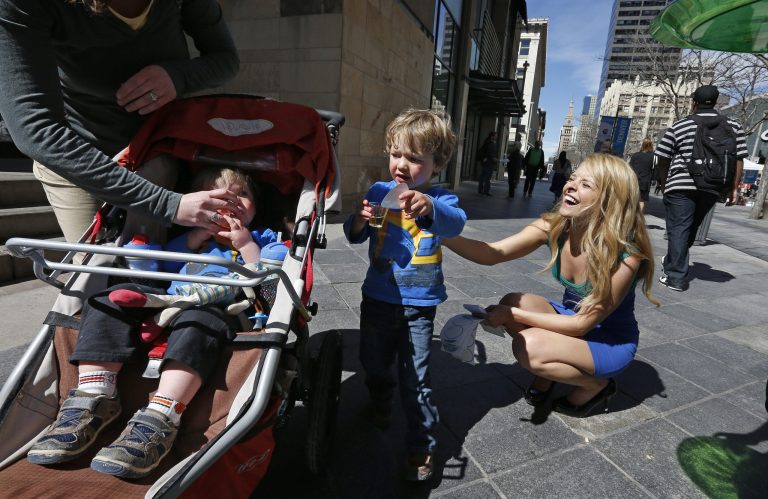 Model Meghan McMahon laughs after giving a sticker to Iggy Cole, age 3, who gave it to his baby brother August, as McMahon handed out literature and juice shots on an outdoor pedestrian mall, encouraging the public to get health coverage under the Affordable Care Act, during a promotional campaign launched by Colorado HealthOP, a independent non-profit health care co-op, in Denver, Thursday March 20, 2014. More than 250,000 Coloradans have become covered through the state-run insurance exchange since enrollment began October 1, 2013, and those who still do not have health insurance have two more weeks to get coverage or pay a fine. (AP Photo/Brennan Linsley)