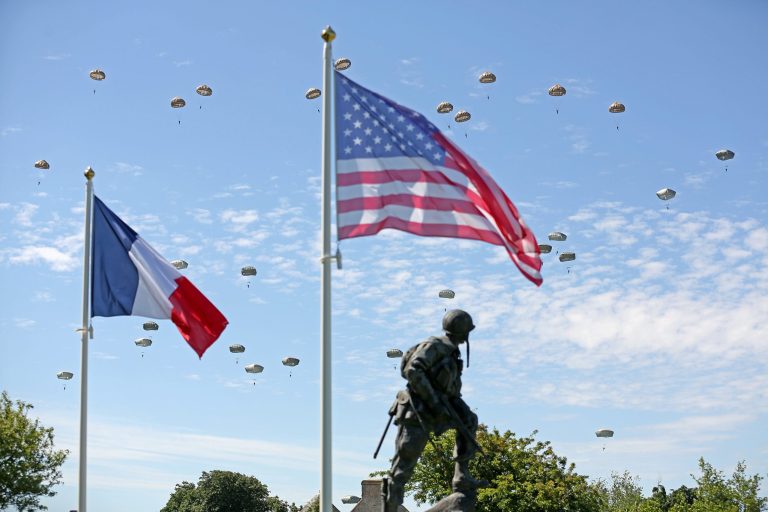 Paratroopers are dropped near the Normandy village of Sainte Mere Eglise, western France, during a mass air drop, Sunday June 8, 2014, as part of commemorations of the 70 anniversary of the D-Day landing. World leaders and veterans gathered by the beaches of Normandy on Friday to mark the 70th anniversary of the World War II D-Day landings. Visible at foreground is bronze sculpture Iron Mike, a monument dedicated to the American airborne soldiers who fought on the D Day.(AP Photo/Remy de la Mauviniere)